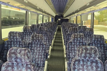 Interior of an empty coach bus showing rows of patterned seats and overhead luggage compartments.
