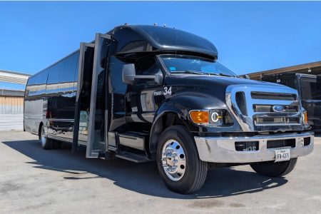 A black Ford passenger bus with its door open is parked in a lot on a sunny day.