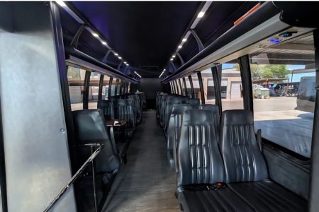 Interior of an empty shuttle bus with rows of black seats and overhead lighting, parked at a lot.