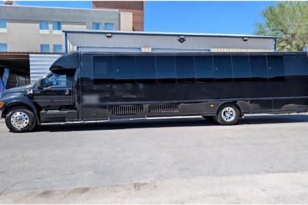 A large black party bus is parked outdoors near a building on a clear day.