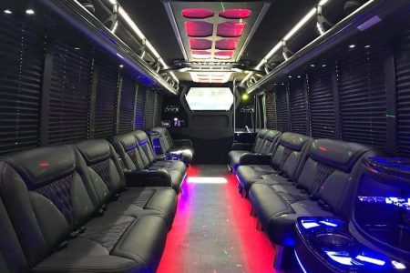 Interior of a luxury party bus with black leather seats, neon lighting, and entertainment screens along the walls and ceiling.