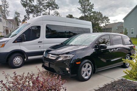 A black minivan and a white passenger van are parked side by side on a residential driveway.
