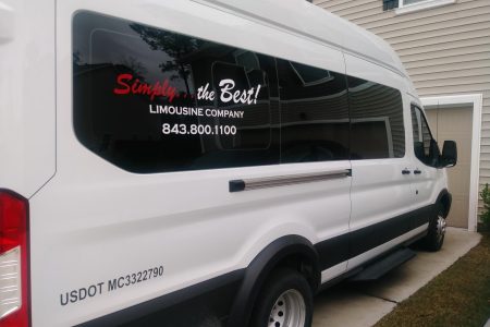 White limousine company van parked in a driveway, displaying company name and contact number on the side window.